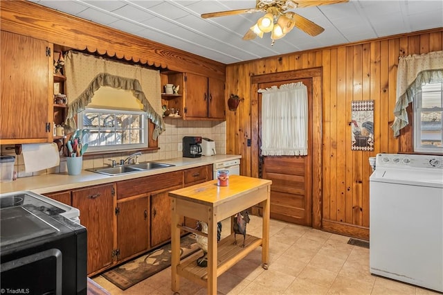 kitchen featuring washer / dryer, sink, wood walls, ceiling fan, and backsplash