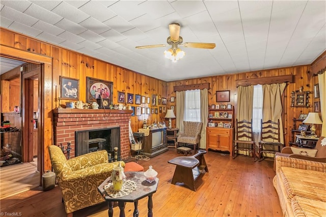 living room with ceiling fan, hardwood / wood-style floors, a fireplace, and wood walls