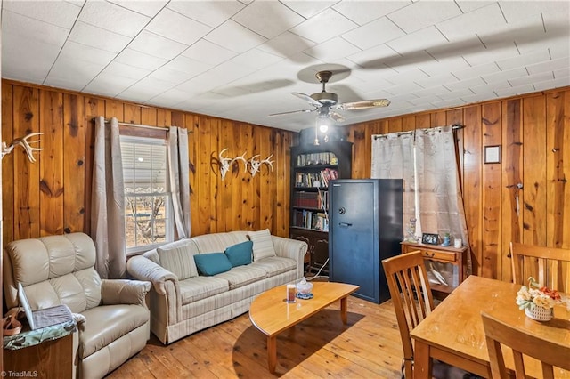 living room with ceiling fan, light hardwood / wood-style floors, and wood walls