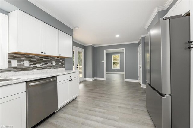 kitchen with light hardwood / wood-style floors, ornamental molding, white cabinetry, appliances with stainless steel finishes, and light stone countertops