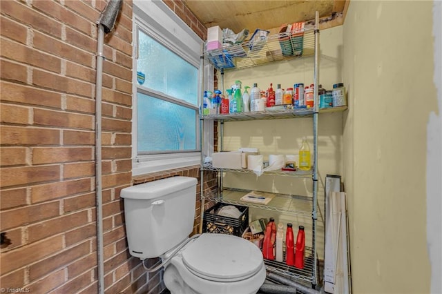 bathroom with toilet and brick wall