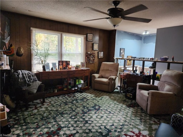 living area featuring carpet floors, wood walls, a textured ceiling, and ceiling fan