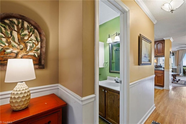 hall with sink, crown molding, a textured ceiling, and light hardwood / wood-style floors