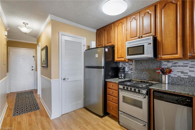 kitchen featuring stainless steel appliances, dark stone counters, decorative backsplash, ornamental molding, and light hardwood / wood-style flooring