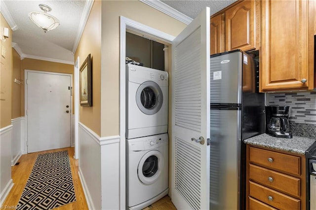 clothes washing area with stacked washer and dryer, crown molding, a textured ceiling, and light hardwood / wood-style flooring