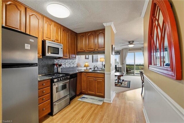 kitchen with appliances with stainless steel finishes, dark stone counters, decorative backsplash, light wood-type flooring, and ceiling fan