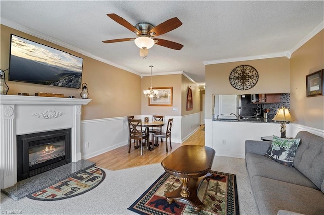 living room with ceiling fan with notable chandelier, light hardwood / wood-style floors, a textured ceiling, and crown molding