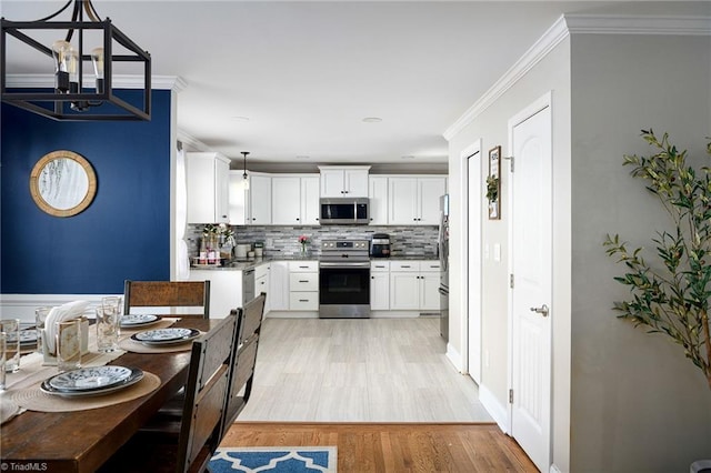 kitchen with backsplash, white cabinets, ornamental molding, decorative light fixtures, and stainless steel appliances