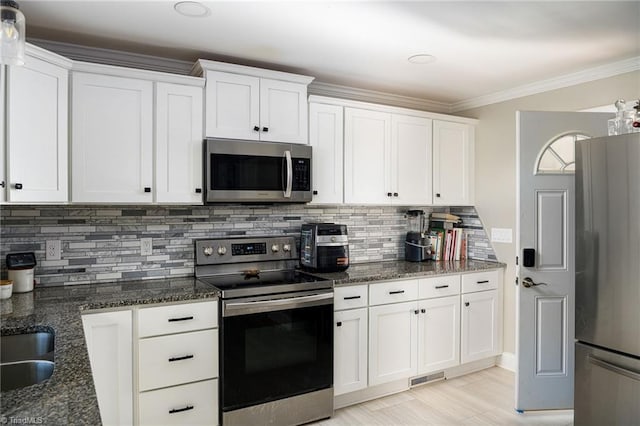 kitchen with tasteful backsplash, ornamental molding, stainless steel appliances, dark stone countertops, and white cabinetry