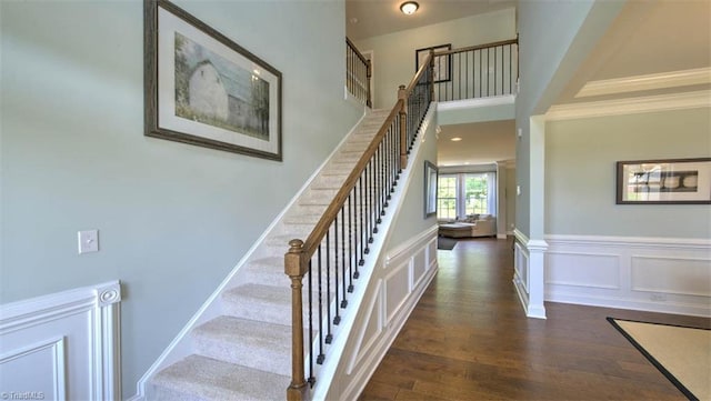 stairs with a towering ceiling, wood-type flooring, and ornamental molding