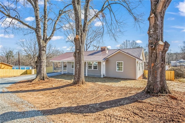 ranch-style home featuring driveway, metal roof, a chimney, and fence