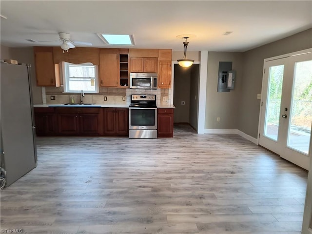 kitchen featuring stainless steel appliances, a sink, light countertops, light wood-type flooring, and decorative backsplash