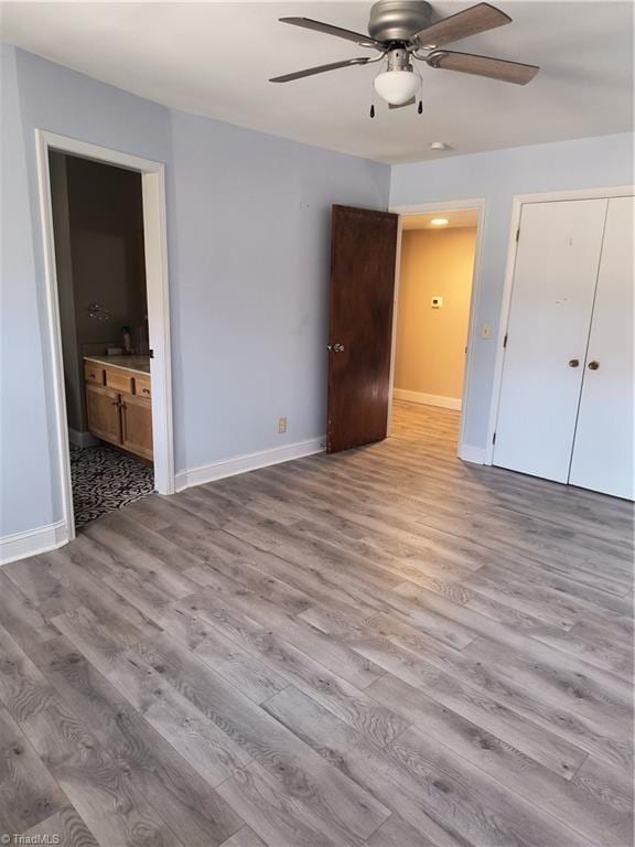 unfurnished bedroom with ensuite bath, wood finished floors, a ceiling fan, and baseboards