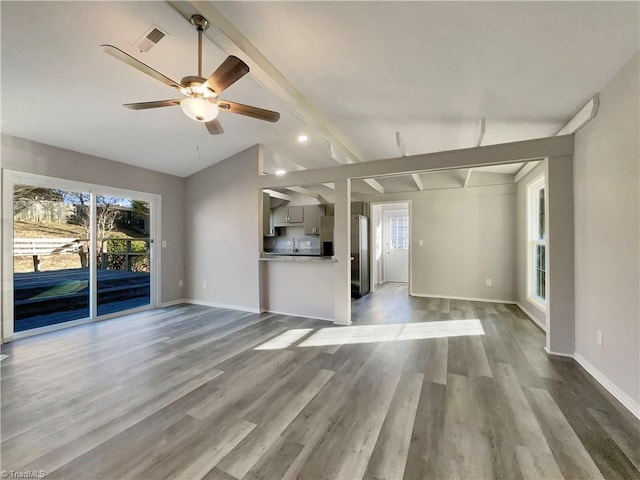 unfurnished living room featuring ceiling fan, hardwood / wood-style floors, vaulted ceiling with beams, and a healthy amount of sunlight