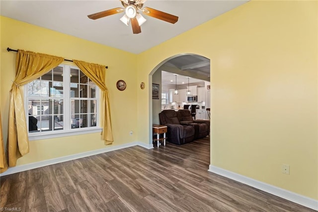 empty room featuring dark wood-type flooring, arched walkways, and baseboards