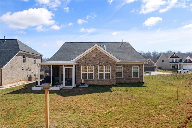 rear view of house with a sunroom, brick siding, a lawn, and roof with shingles