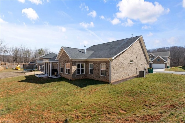 rear view of property featuring a trampoline, brick siding, a yard, and central AC unit