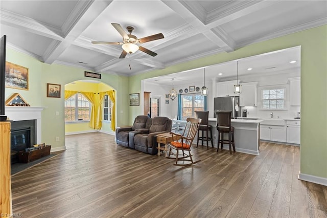 living area with arched walkways, dark wood-type flooring, coffered ceiling, and baseboards