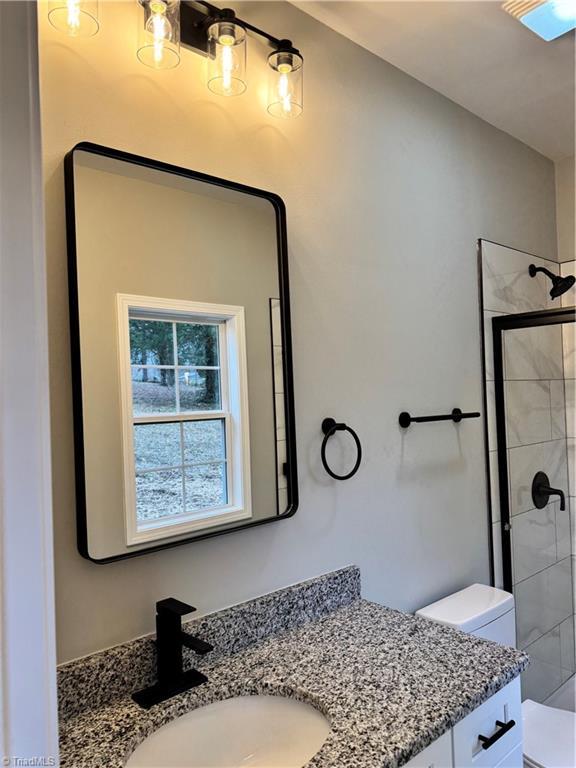 bathroom featuring a tile shower, vanity, and toilet