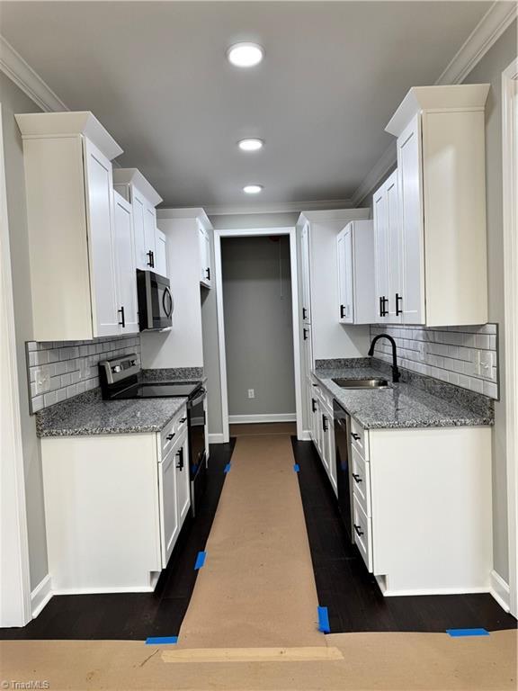 kitchen featuring sink, white cabinets, dark stone counters, ornamental molding, and stainless steel appliances