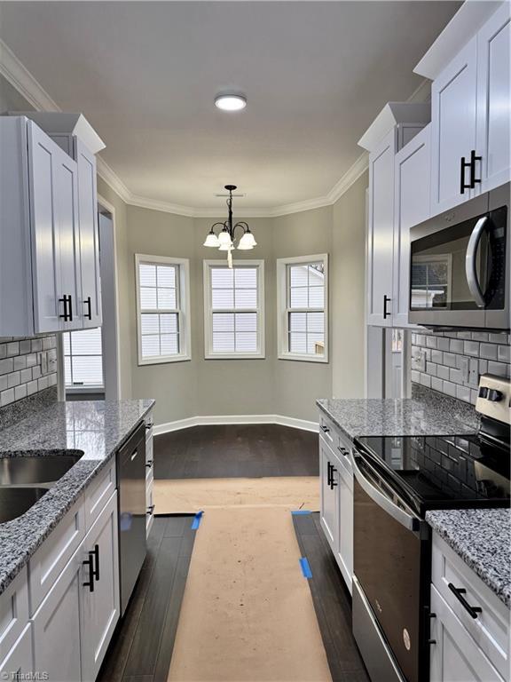 kitchen featuring white cabinetry, stainless steel appliances, crown molding, and pendant lighting