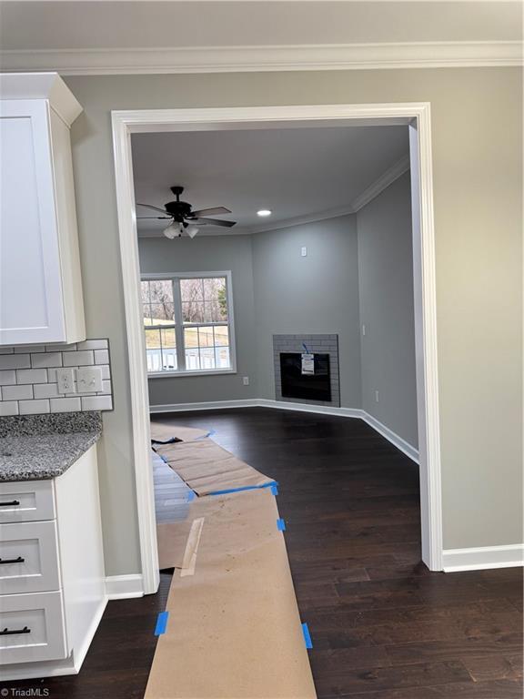 unfurnished living room with dark wood-type flooring, ceiling fan, and crown molding