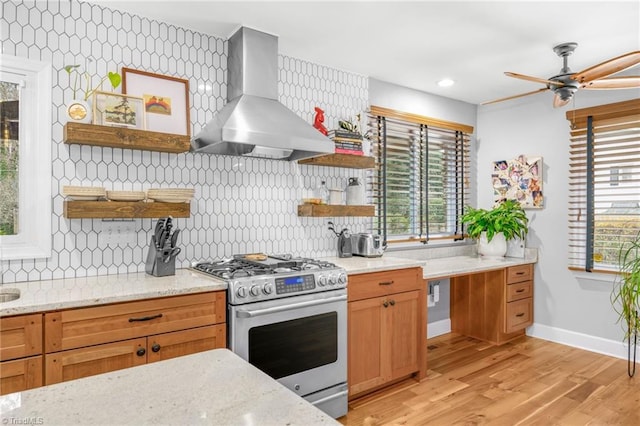 kitchen with light stone counters, open shelves, light wood-style flooring, wall chimney exhaust hood, and stainless steel gas stove