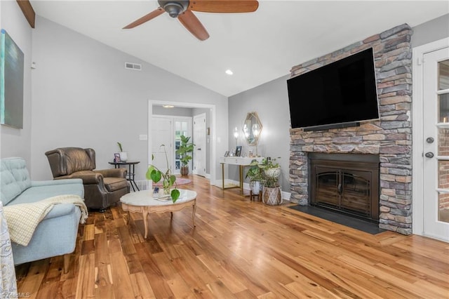 living area featuring vaulted ceiling, visible vents, a stone fireplace, and wood finished floors