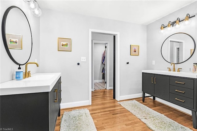 full bath featuring wood finished floors, two vanities, baseboards, and a sink