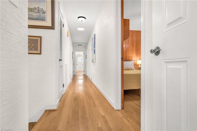 corridor with light wood-type flooring and baseboards