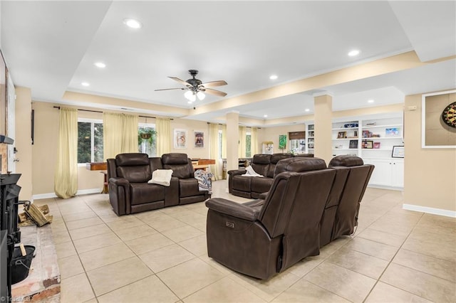 living room featuring light tile patterned floors, built in features, baseboards, ceiling fan, and a raised ceiling