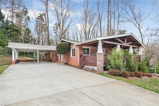 view of side of home featuring a porch, a carport, brick siding, and driveway