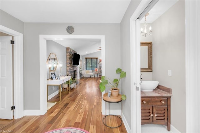 hall with baseboards, an inviting chandelier, lofted ceiling, a sink, and light wood-style floors