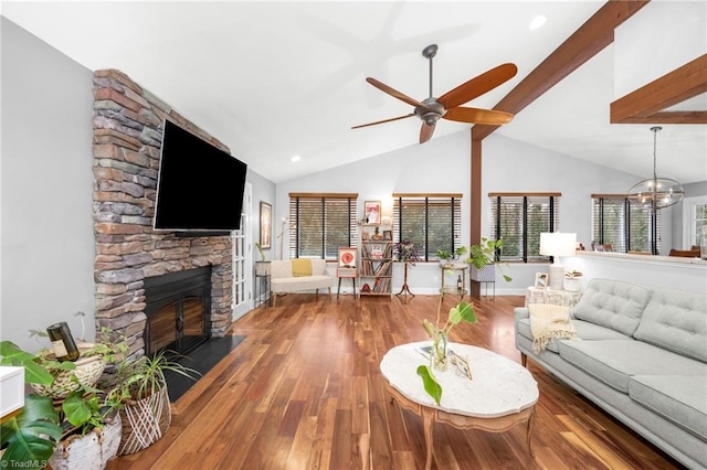 living area featuring baseboards, lofted ceiling with beams, a stone fireplace, ceiling fan with notable chandelier, and wood finished floors