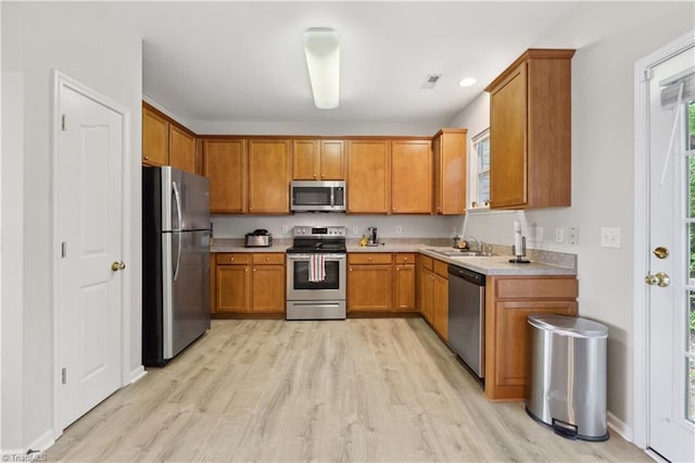 kitchen with stainless steel appliances, brown cabinetry, light wood-type flooring, and a sink