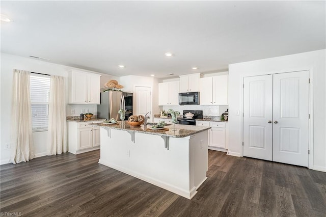 kitchen featuring a breakfast bar, stone counters, black appliances, white cabinets, and a center island with sink