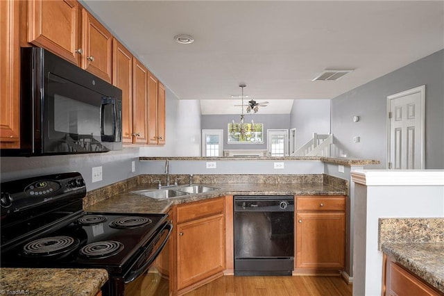 kitchen with black appliances, sink, a notable chandelier, kitchen peninsula, and light wood-type flooring