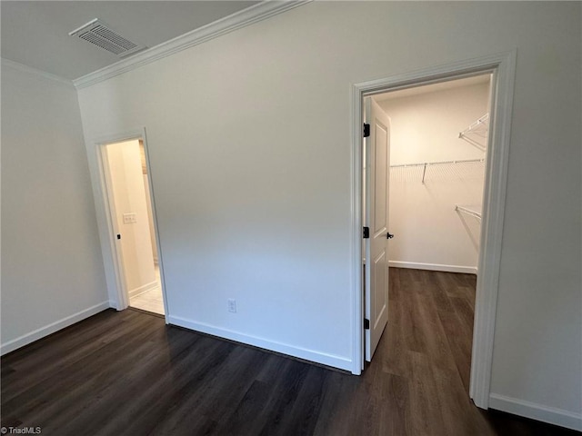 unfurnished bedroom with a spacious closet, a closet, dark wood-type flooring, and ornamental molding