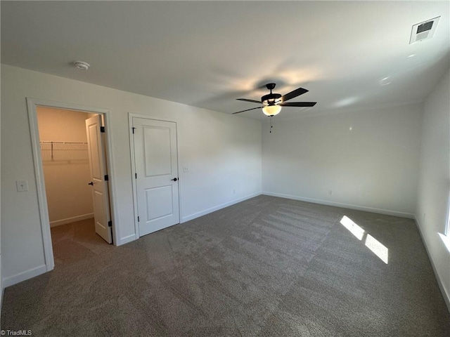 unfurnished bedroom featuring ceiling fan, dark carpet, a walk in closet, and a closet