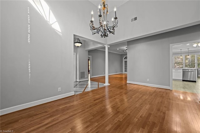 unfurnished dining area featuring ceiling fan with notable chandelier, decorative columns, high vaulted ceiling, and wood-type flooring