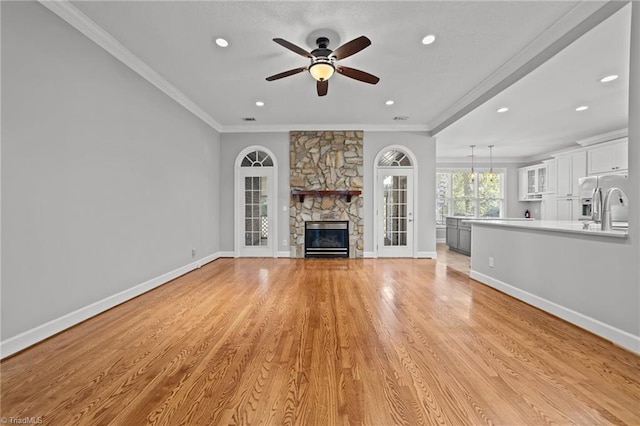 unfurnished living room featuring crown molding, ceiling fan, a stone fireplace, and light hardwood / wood-style flooring