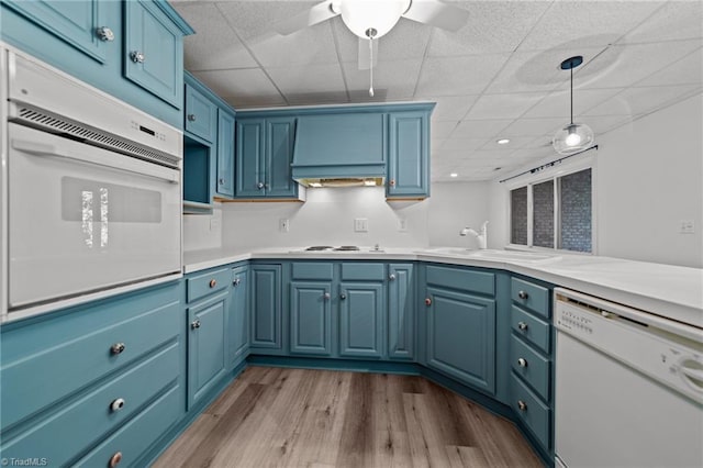 kitchen with ceiling fan, white appliances, blue cabinetry, light hardwood / wood-style flooring, and hanging light fixtures