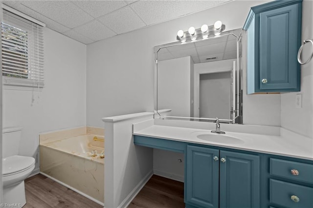 bathroom featuring a drop ceiling, toilet, hardwood / wood-style floors, a bath, and vanity