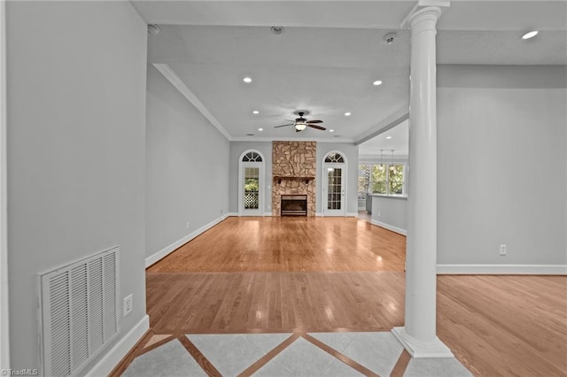 unfurnished living room with ceiling fan, a stone fireplace, light hardwood / wood-style flooring, decorative columns, and crown molding