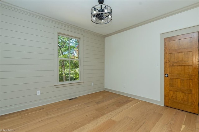 empty room with wood walls, ornamental molding, and light wood-type flooring