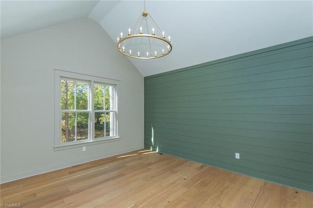 empty room featuring wood walls, lofted ceiling, light hardwood / wood-style flooring, and an inviting chandelier