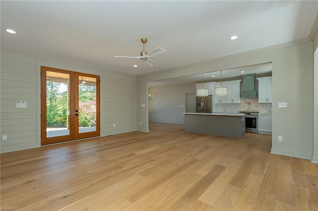 unfurnished living room featuring wood walls, french doors, light hardwood / wood-style flooring, ornamental molding, and ceiling fan