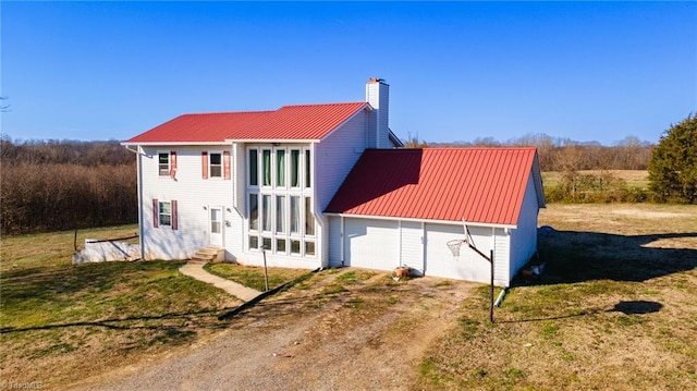 exterior space featuring metal roof, a garage, driveway, a chimney, and a front yard