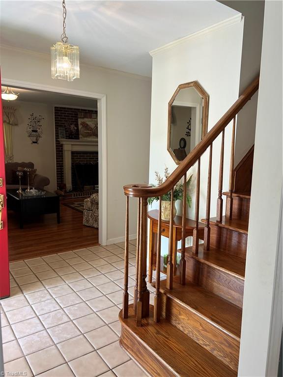 209 Cedar Ln, North Wilkesboro, NC 28659 - stairs featuring crown molding, tile patterned flooring, a chandelier, and a fireplace