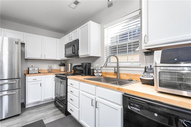 kitchen featuring wood counters, light wood-type flooring, sink, black appliances, and white cabinetry